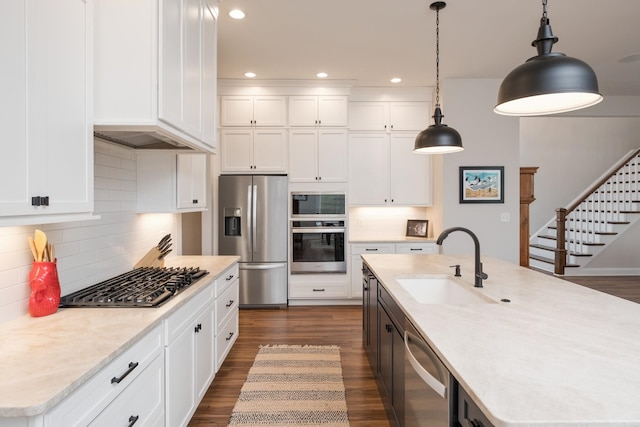 kitchen with an island with sink, appliances with stainless steel finishes, white cabinets, a sink, and dark wood-style floors