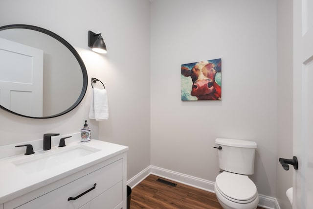 half bath featuring visible vents, baseboards, toilet, wood finished floors, and vanity
