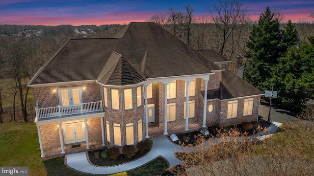 view of front of house featuring brick siding, a balcony, french doors, and a lawn
