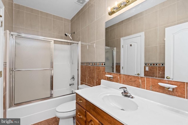 full bath with shower / bath combination with glass door, vanity, visible vents, toilet, and tile walls