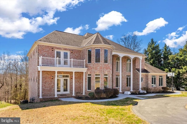 view of front facade with brick siding, french doors, a front yard, and a balcony