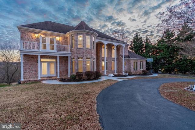 view of front of house featuring a balcony, curved driveway, french doors, a front yard, and brick siding