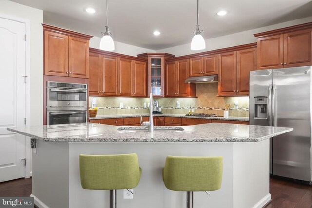 kitchen featuring stainless steel appliances, an island with sink, decorative light fixtures, a breakfast bar, and sink