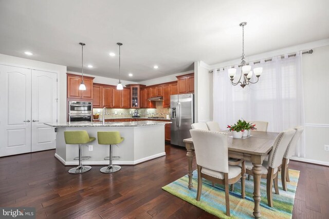 kitchen featuring a center island with sink, stainless steel appliances, decorative light fixtures, and dark hardwood / wood-style floors