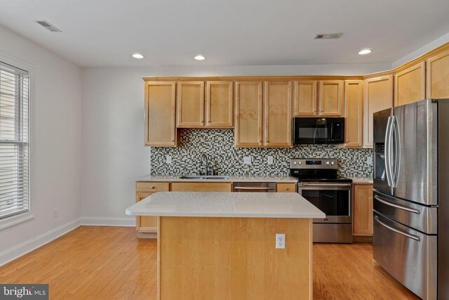 kitchen featuring stainless steel appliances, a kitchen island, sink, and light wood-type flooring