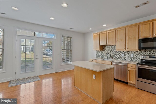 kitchen featuring sink, light hardwood / wood-style flooring, appliances with stainless steel finishes, a kitchen island, and decorative backsplash