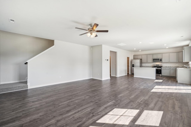 unfurnished living room featuring visible vents, dark wood-type flooring, baseboards, stairs, and a ceiling fan