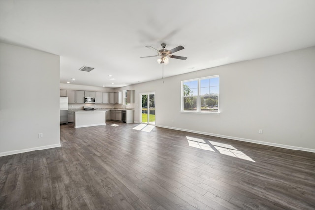 unfurnished living room with dark wood-style floors, visible vents, a ceiling fan, and baseboards