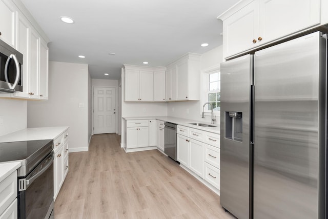 kitchen with light countertops, light wood-style floors, white cabinets, stainless steel appliances, and a sink