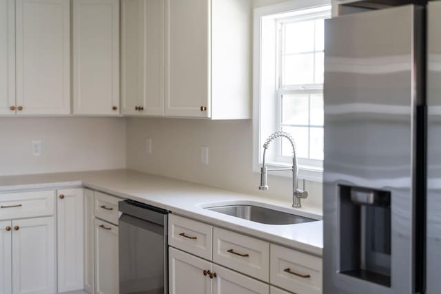 kitchen with a sink, stainless steel appliances, light countertops, and white cabinetry