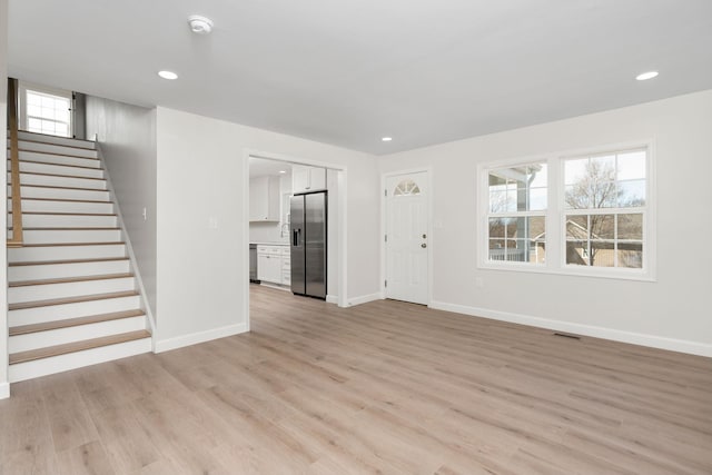 unfurnished living room with visible vents, light wood-style flooring, stairs, and baseboards