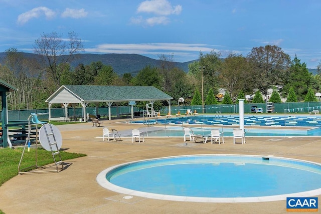 community pool featuring a gazebo, a patio area, fence, a mountain view, and a water slide