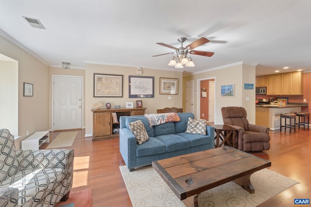 living area with baseboards, light wood-style flooring, visible vents, and crown molding