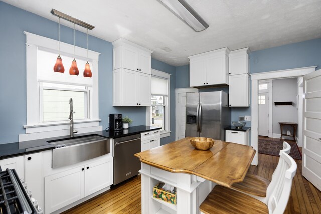 kitchen with pendant lighting, a sink, wood-type flooring, appliances with stainless steel finishes, and white cabinets