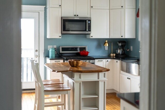 kitchen with white cabinets, appliances with stainless steel finishes, a center island, and light wood-type flooring