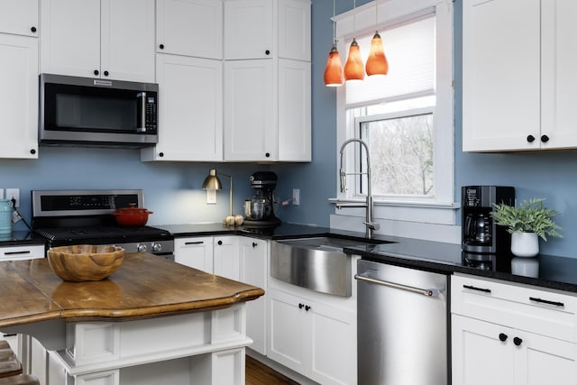 kitchen with dark countertops, white cabinets, appliances with stainless steel finishes, and a sink