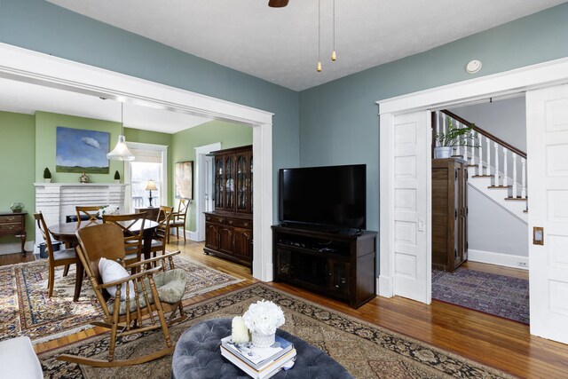 living area featuring a ceiling fan, wood finished floors, a fireplace, baseboards, and stairs