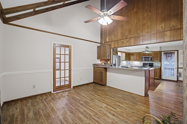 kitchen with stone counters, appliances with stainless steel finishes, high vaulted ceiling, wood-type flooring, and kitchen peninsula