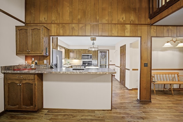 kitchen with wood walls, decorative light fixtures, kitchen peninsula, stainless steel appliances, and light hardwood / wood-style floors