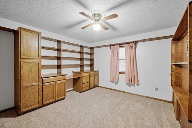 unfurnished office with a textured ceiling, built in desk, light colored carpet, and ceiling fan