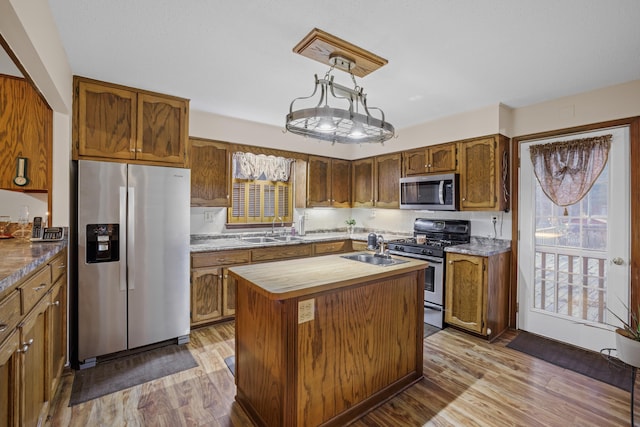 kitchen with a kitchen island, decorative light fixtures, sink, stainless steel appliances, and light hardwood / wood-style flooring