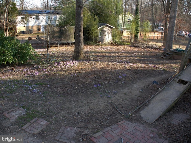 view of yard featuring a shed, a trampoline, fence, and an outdoor structure