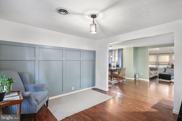 living area featuring visible vents, a decorative wall, and wood finished floors