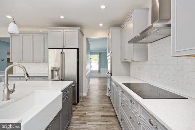 kitchen featuring hanging light fixtures, wood finished floors, black electric cooktop, a sink, and wall chimney exhaust hood