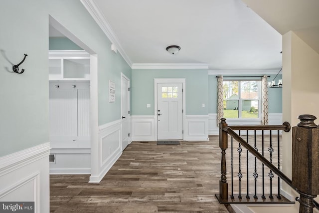 entrance foyer with ornamental molding, a decorative wall, wood finished floors, and a wainscoted wall