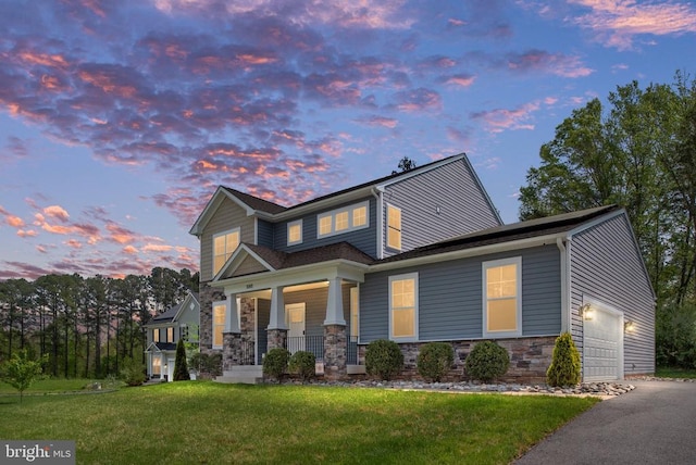 craftsman-style house with a garage, aphalt driveway, stone siding, a porch, and a yard