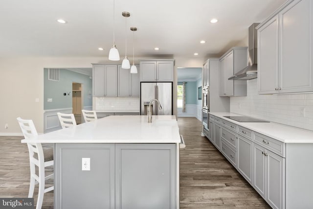kitchen with wall chimney range hood, a breakfast bar area, tasteful backsplash, wood finished floors, and stainless steel appliances