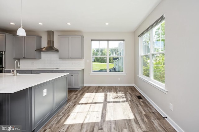 kitchen featuring wall chimney range hood, black electric cooktop, gray cabinetry, and light countertops