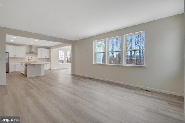 unfurnished living room featuring recessed lighting, baseboards, a sink, and light wood finished floors