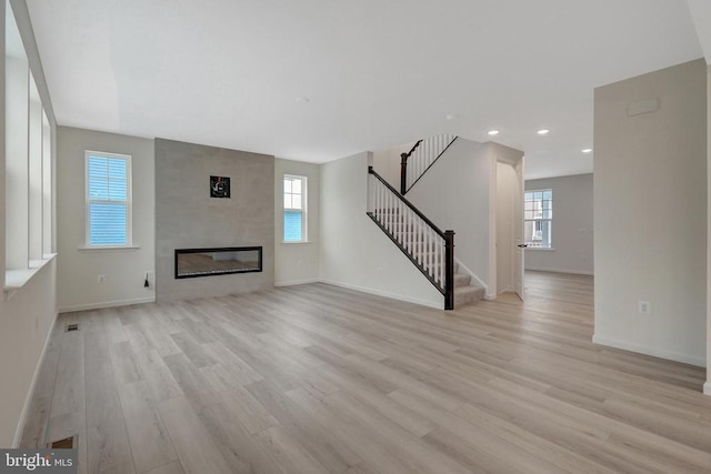 unfurnished living room featuring a large fireplace, baseboards, stairway, light wood-style floors, and recessed lighting