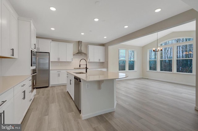 kitchen with light countertops, appliances with stainless steel finishes, white cabinets, a sink, and wall chimney range hood