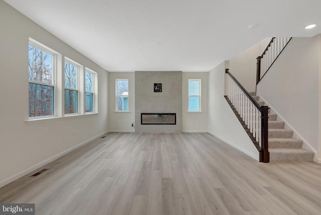 unfurnished living room featuring a fireplace, visible vents, light wood-style flooring, baseboards, and stairs