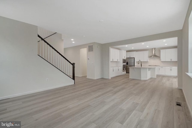 unfurnished living room with light wood finished floors, stairway, visible vents, and baseboards