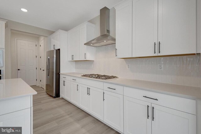 kitchen with wall chimney exhaust hood, light wood-style flooring, stainless steel appliances, light countertops, and white cabinetry