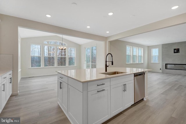 kitchen with an island with sink, open floor plan, light countertops, stainless steel dishwasher, and a sink