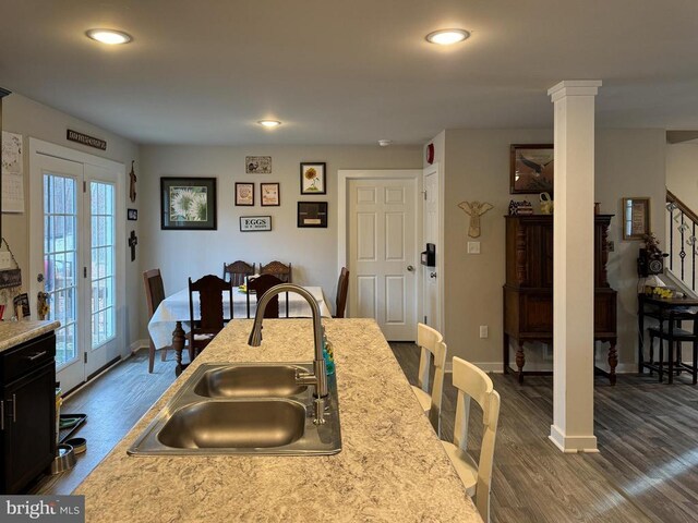 kitchen with decorative columns, light stone countertops, sink, and dark hardwood / wood-style floors