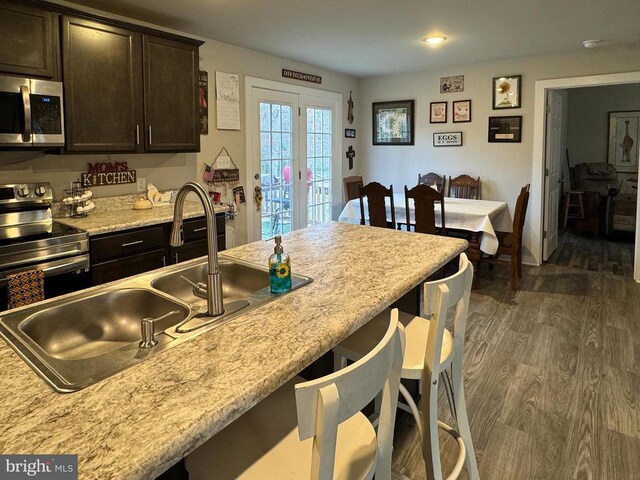 kitchen featuring sink, appliances with stainless steel finishes, dark brown cabinets, dark hardwood / wood-style floors, and light stone counters