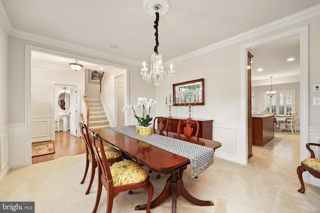 dining area featuring a wainscoted wall, a decorative wall, ornamental molding, a chandelier, and stairs