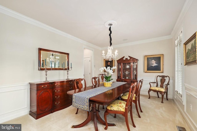 dining space with light carpet, a wainscoted wall, ornamental molding, an inviting chandelier, and a decorative wall