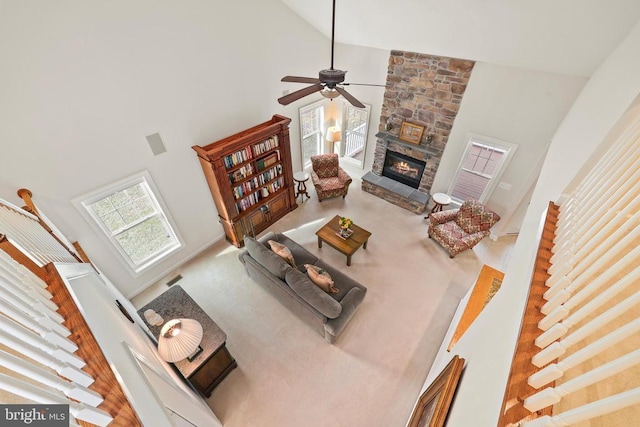 living area with visible vents, ceiling fan, carpet flooring, a stone fireplace, and high vaulted ceiling