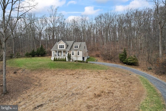 view of front facade with a porch, a front yard, driveway, and a forest view