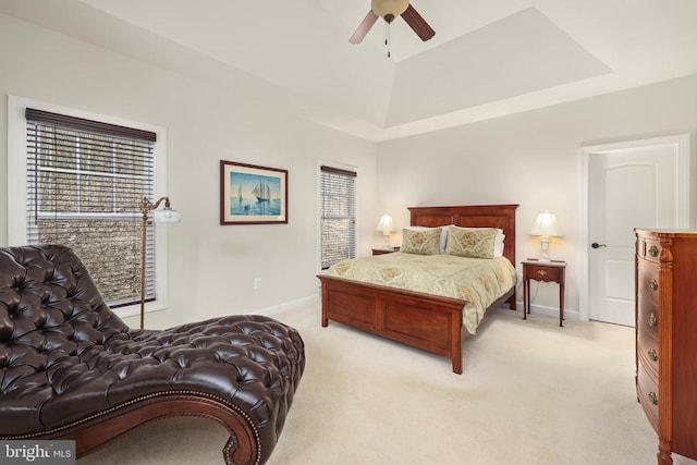 bedroom featuring a raised ceiling, light carpet, ceiling fan, and baseboards