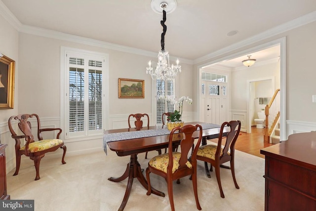 dining area with stairway, light colored carpet, crown molding, and wainscoting