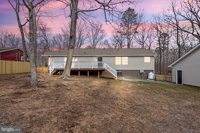 back of house at dusk with stairs, a deck, and fence