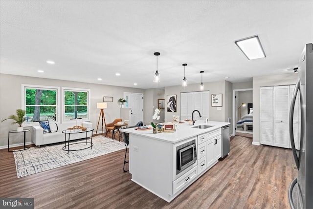 kitchen featuring an island with sink, appliances with stainless steel finishes, light countertops, pendant lighting, and a sink