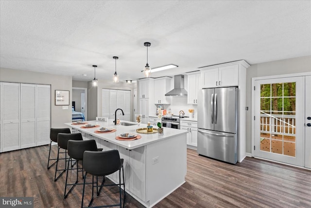 kitchen featuring white cabinets, an island with sink, wall chimney exhaust hood, appliances with stainless steel finishes, and a sink